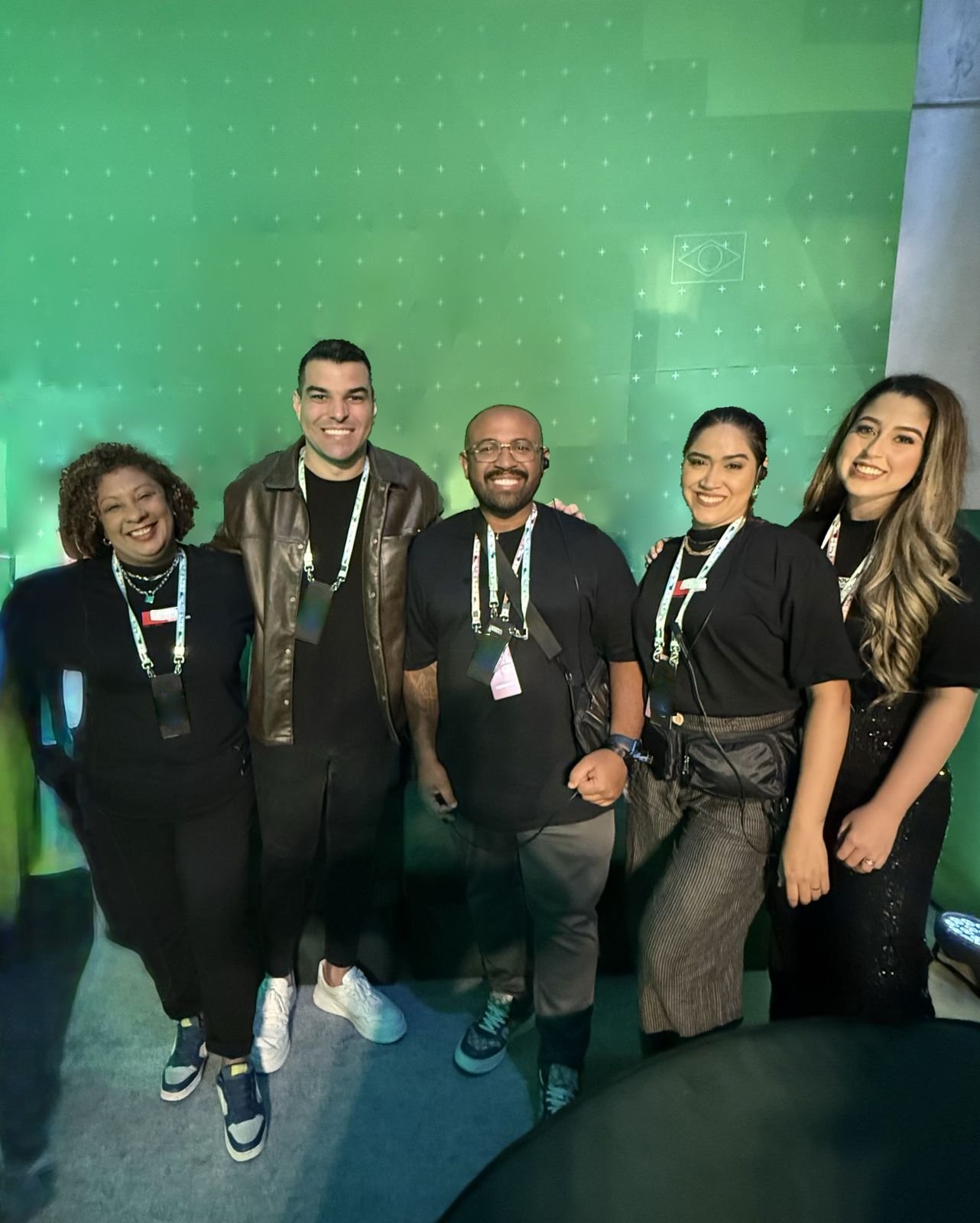 The crew together in front of a green wall, with the Brazilian flag
